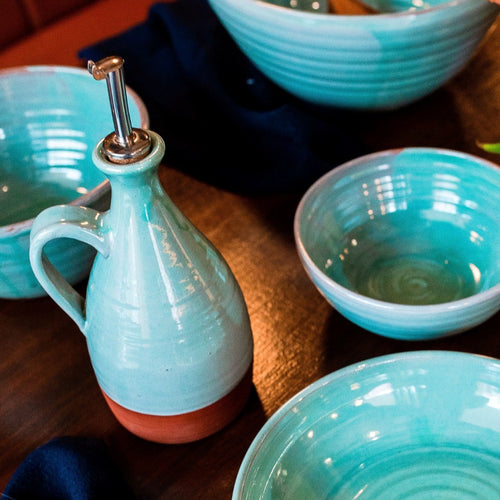 Turquoise oil pourer and 4 bowls sitting on a dark wooden table