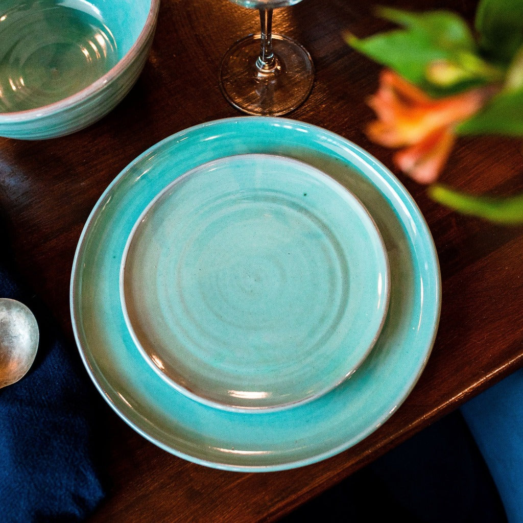 Turquoise side plate sitting on a turquoise dinner plate on a dark wooden table.