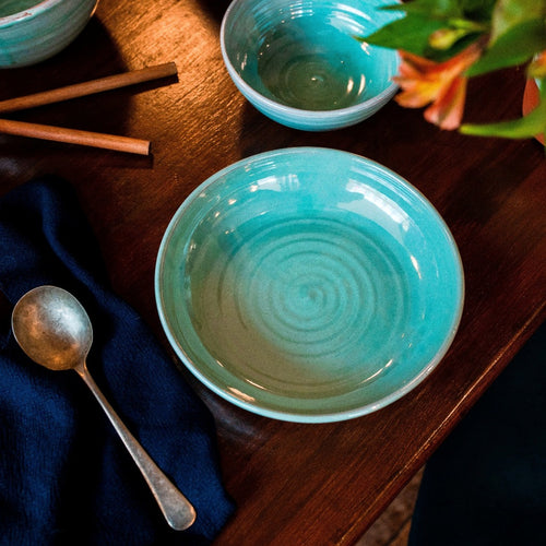 Turquoise pasta bowl on a dark table with navy napkin and soup spoon.