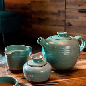 Turquoise mik jug, sugar bowl, teapot sitting on a wooden table.