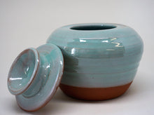 Load image into Gallery viewer, Turquoise jar with a lid leaning against iton a white background.
